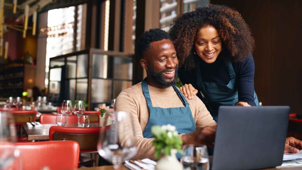 Restaurant owners checking their social media marketing strategy on a laptop, reflecting how social media helps small businesses engage with customers.