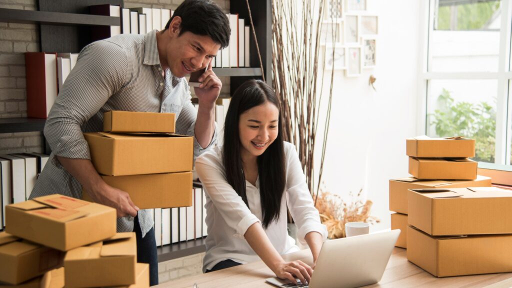 Small business owners packing products and using a laptop to manage online orders, highlighting the use of social media management in e-commerce.